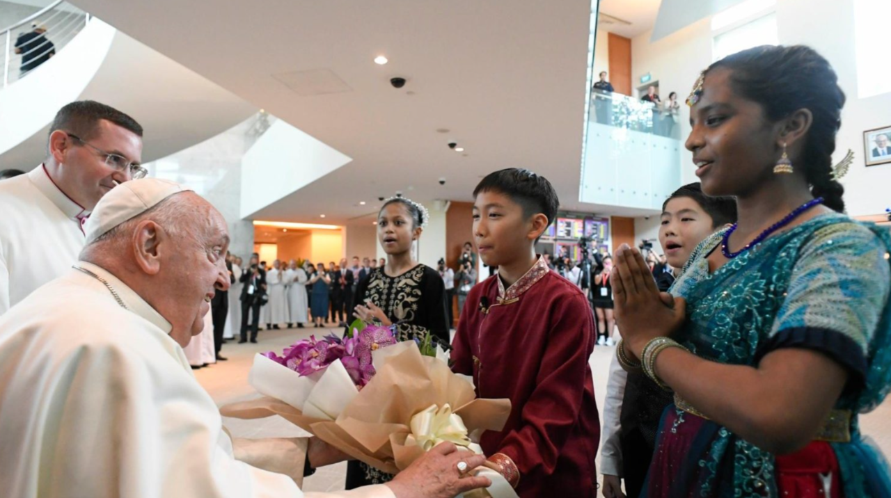 Cuatro niños vestidos con trajes tradicionales dan la bienvenida al Papa a Singapur.