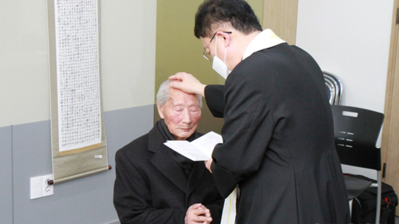 El Padre Joo Young-don impone las manos sobre el anciano Ahn.